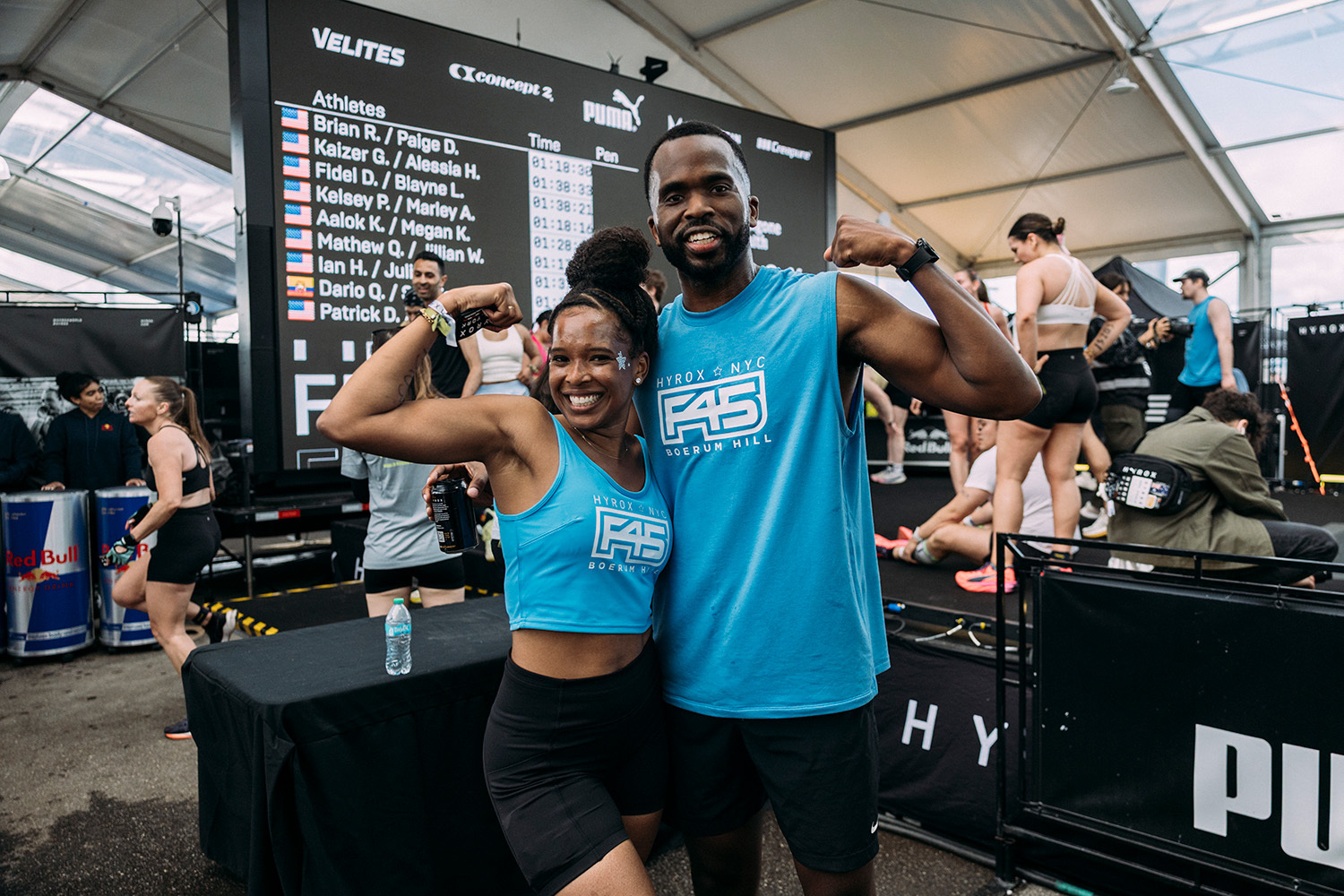 Two F45 members in blue F45 singlets flexing after a HYROX race