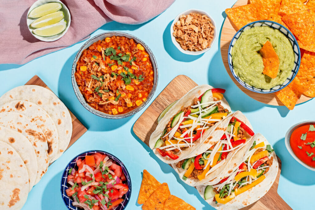A table full of different Mexican food with tacos, salsa, and guacamole